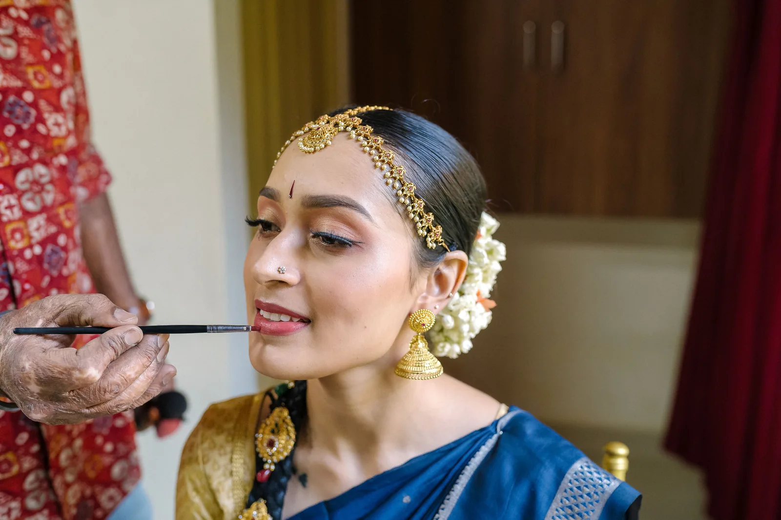 Bride in a blue silk saree with jasmine in her hair, a quiet profile while her make-up is finished