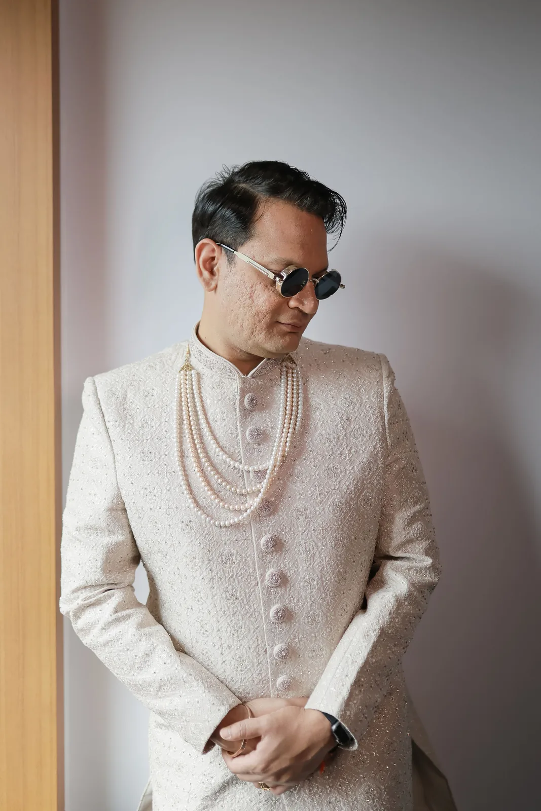Groom in an ivory sherwani and sunglasses in window light