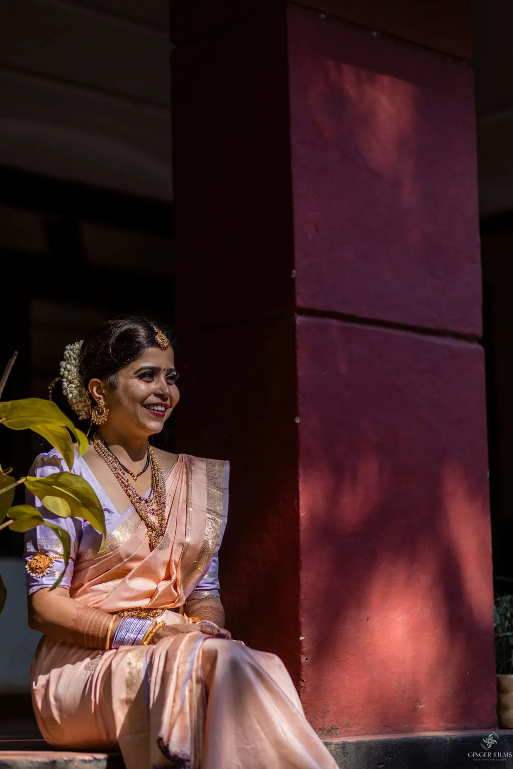 Bride in a pastel silk saree laughing against a deep red wall