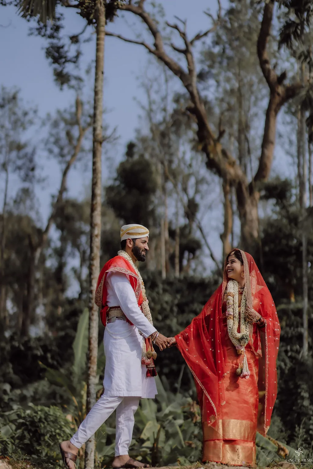 Bride in red and groom in white walking hand in hand through hill-country trees